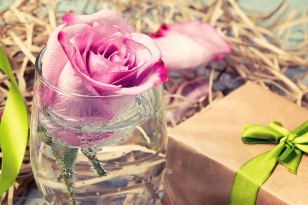 Rosa rosa en un vaso con agua y decoraciones sobre la mesa — Foto de Stock