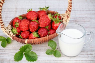 Bir sepet içinde taze olgun çilek ve bir yaz gününde açık havada ahşap bir masada iogurt