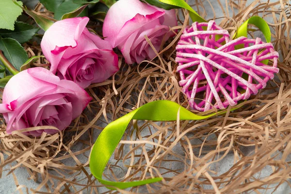 Ramo de rosas rosadas y un corazón de mimbre con decoraciones en la mesa un concepto de amor y felicitaciones por un ser querido — Foto de Stock