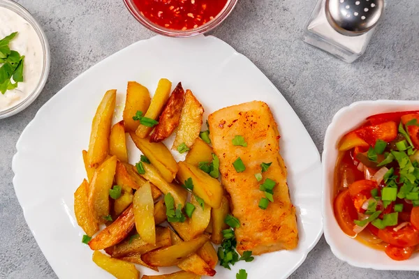 Pescado frito y patatas fritas en un plato blanco en la mesa de la cocina con salsa de tomate, salsa tártara y ensalada de verduras en vinagre - foto, imagen — Foto de Stock