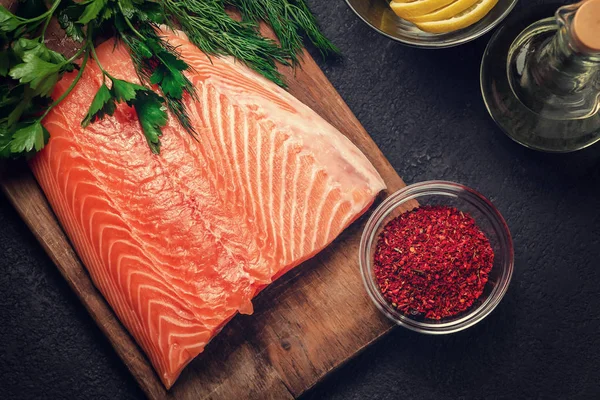 Piece of salmon fillet on a wooden cutting board with ingredients for its further preparation, top view - photo, image — Stock Photo, Image