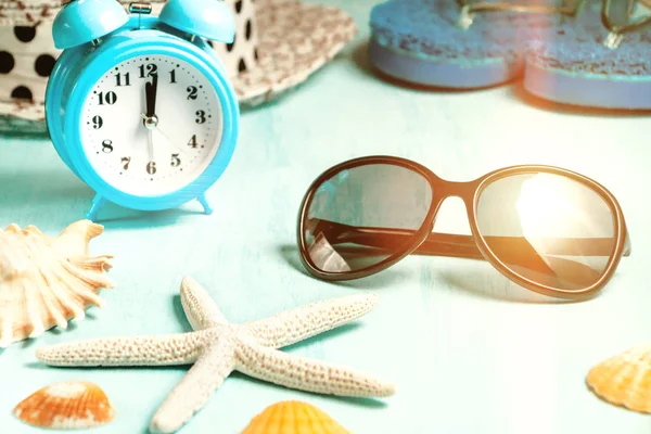 Mušle, budík a plážové příslušenství na modrém stole-letní prázdniny a v době dovolené — Stock fotografie