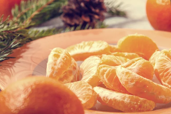 Plusieurs tranches de mandarine pelées sur une assiette orange avec des branches d'arbre et un cône une composition traditionnelle de Noël et du Nouvel An en Russie — Photo