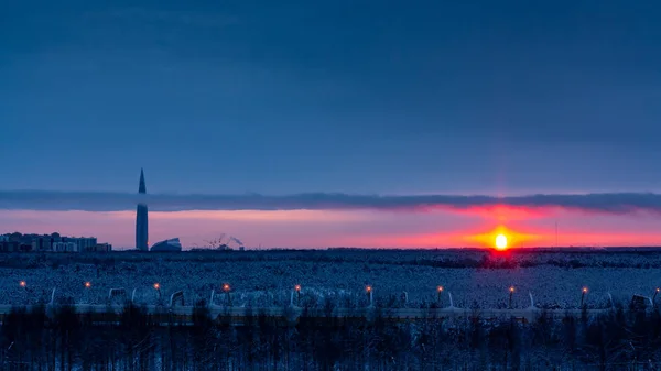 Kleurrijke zonsondergang in de bewolkte hemel boven een besneeuwd bos aan de rand van de stad — Stockfoto