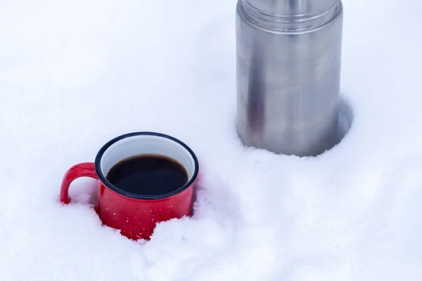 Tazza di metallo rosso con caffè versato da un thermos sulla neve bianca pura nella foresta mentre si cammina — Foto Stock