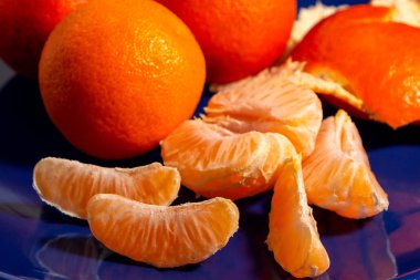 Mavi bir tabak üzerinde birkaç bütün ve soyulmuş olgun mandalina