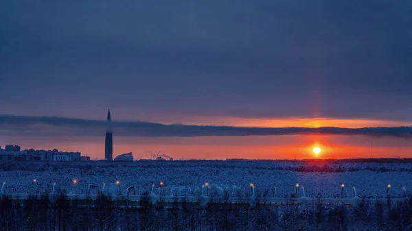 街の郊外の雪の森の上に曇った空にカラフルな夕日 — ストック写真