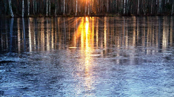 Strahlen der untergehenden Sonne spiegeln sich im Flusswasser, das mit dem ersten Eis bedeckt wurde — Stockfoto