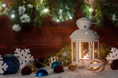 Yanan bir mum ile Beyaz fener ahşap bir duvar, Noel ağacı dalları ve ışıklar arka planda Noel süslemeleri ile çevrili kar duruyor