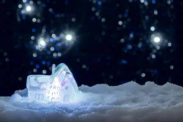 Izzó játék ház a hóban a háttérben a karácsonyi fények. Ünnepi, karácsonyi vagy újévi koncepció — Stock Fotó