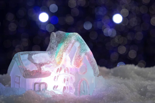 Izzó játék ház a hóban a háttérben a karácsonyi fények. Ünnepi, karácsonyi vagy újévi koncepció — Stock Fotó