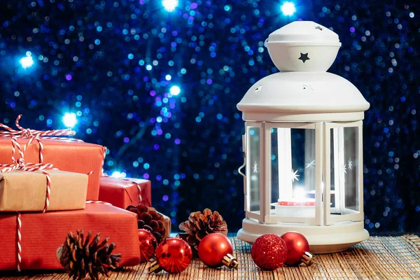 White lantern with a burning candle and boxes with gifts on the background of the Christmas tree with lights. Beautiful christmas or new year background — 스톡 사진