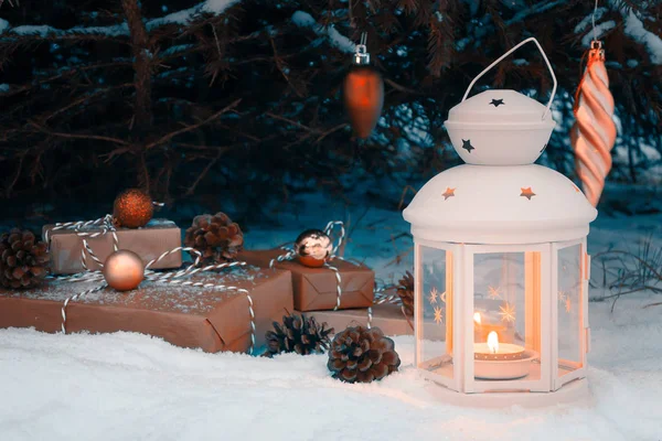 Lanterna con una candela accesa e regali avvolti nella neve sotto l'albero di Natale la vigilia di Natale — Foto Stock