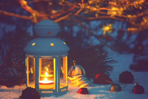 Latarnia z płonącym świecą i dekoracjami świątecznymi na pokrytym śniegiem stole — Zdjęcie stockowe