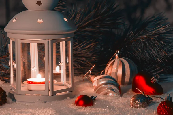 Фонарь с горящей свечой и рождественскими украшениями на заснеженном столе — стоковое фото