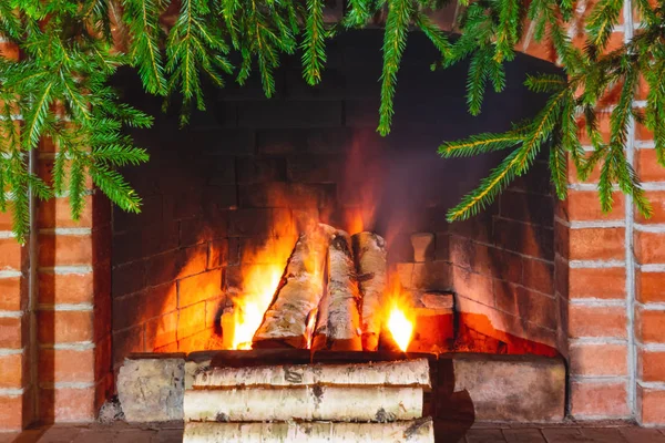 Bois de chauffage brûlant dans une cheminée décorée pour Noël avec des branches d'épinette — Photo