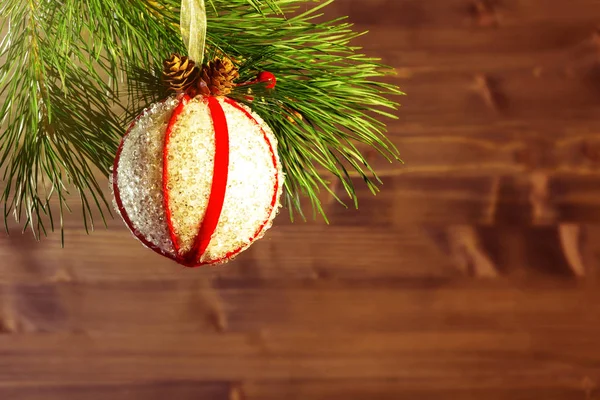 Ramo de uma árvore de Natal decorada com uma bola branca com fitas vermelhas e cones em um fundo de madeira. Espaço de cópia para texto — Fotografia de Stock