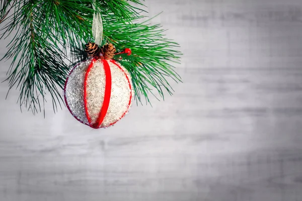 Větev vánočního stromu ozdobená bílou koulí s červenými stuhami a kužele na dřevěném pozadí. Kopírovat prostor pro text — Stock fotografie