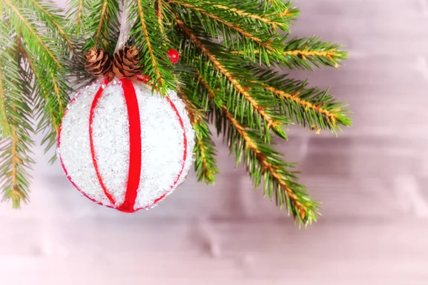 Větev vánočního stromu ozdobená bílou koulí s červenými stuhami a kužele na dřevěném pozadí. Kopírovat prostor pro text — Stock fotografie