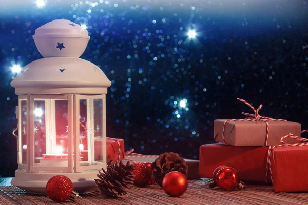 Witte lantaarn met een brandende kaars en dozen met geschenken op de achtergrond van de kerstboom met verlichting. Mooie kerst of nieuwjaar achtergrond — Stockfoto