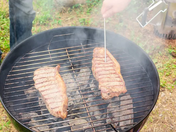 Dwie soczyste steki wołowe są grillowane na okrągłym grillu. Sprawdzenie gotowości mięsa — Zdjęcie stockowe