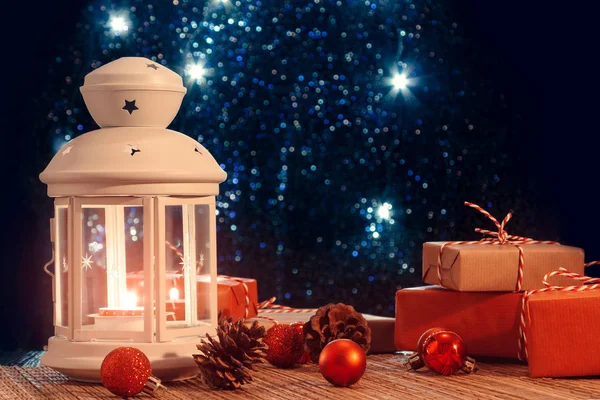 White lantern with a burning candle and boxes with gifts on the background of the Christmas tree with lights. Beautiful christmas or new year background — 스톡 사진