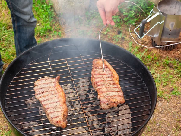Dois bifes de carne suculentos são grelhados em uma grade redonda. Verificação da prontidão da carne — Fotografia de Stock
