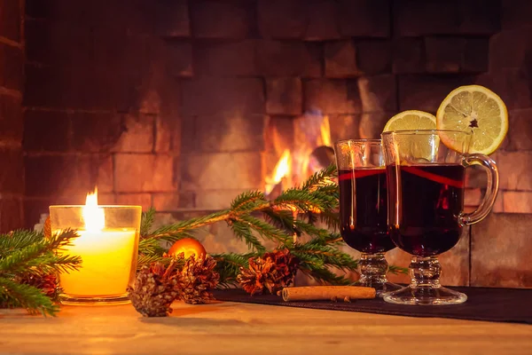 Dois copos com vinho ruminado, uma vela, ramos de abeto com decorações em uma mesa de madeira no contexto de uma lareira ardente. Conceito de Natal romântico — Fotografia de Stock