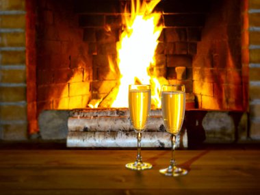 Yanan huş ağacı ile şömine yakınında ahşap bir masada şampanya ile iki bardak