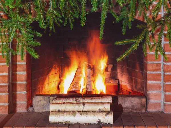 Burning firewood in a fireplace decorated for Christmas with branches of spruce