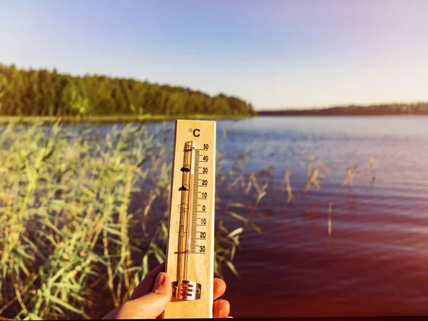 Thermometer showing 30 degrees Celsius of heat against the background of the lake water and the blue sky in sunlight