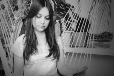 Uzun koyu saçlı güzel kız balkonda bir hamakta oturan bir kitap okur, Bw