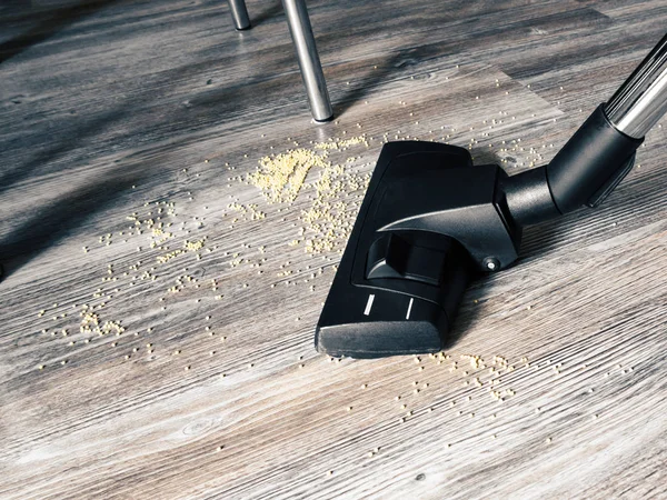 Śmieci na podłodze jest czyszczone za pomocą odkurzacza. W ramie, szczotka z odkurzacza, nogi stołów i krzeseł, podłoga z wzorem do drewna — Zdjęcie stockowe