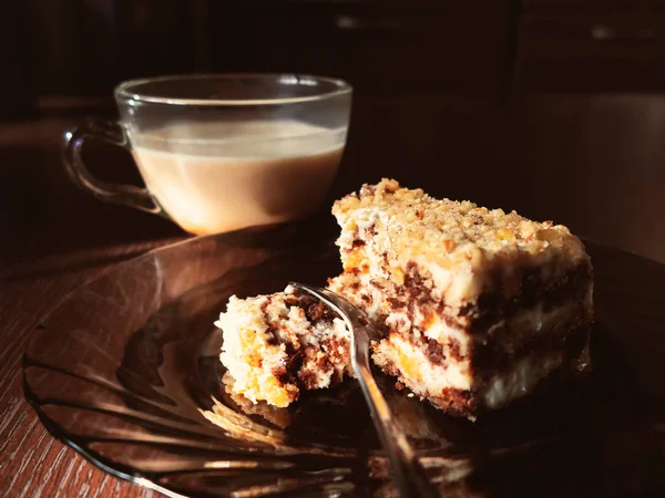 Кусок шоколадного торта на тарелке и чашка кофе с молоком на тёмном деревянном столе на кухне — стоковое фото