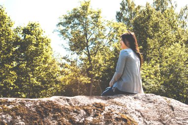 Genç güzel kız büyük bir kayanın üzerinde oturur ve doğaya hayran kalır.