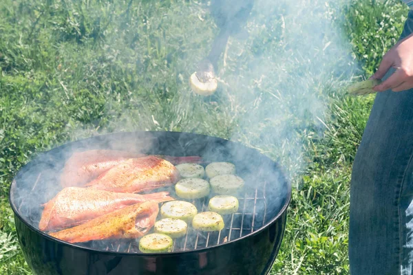 Piknik na świeżym powietrzu w lecie. Gotowanie na okrągłym grillu ryb morskich bas i cukinia plastry — Zdjęcie stockowe