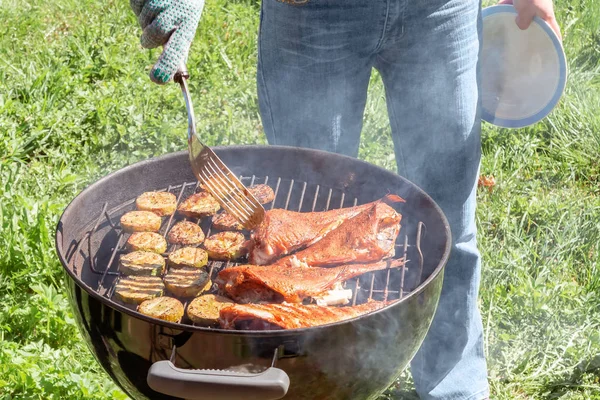 Piquenique ao ar livre no verão. Cozinhar em um peixe grelha redonda robalo e fatias de abobrinha — Fotografia de Stock