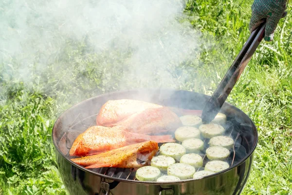 Piknik na świeżym powietrzu w lecie. Gotowanie na okrągłym grillu ryb morskich bas i cukinia plastry — Zdjęcie stockowe