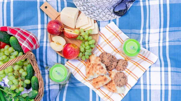 Picnic on the grass on a summer day - basket, grapes, cheese, bread, apples - a concept of summer outdoor recreation