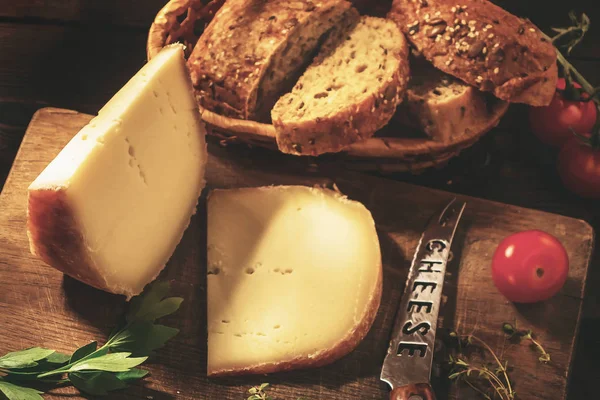 Snijd een plakje harde kaas, peterselie, tijm, kaas mes, graan brood en cherry tomaten op een houten tafel — Stockfoto