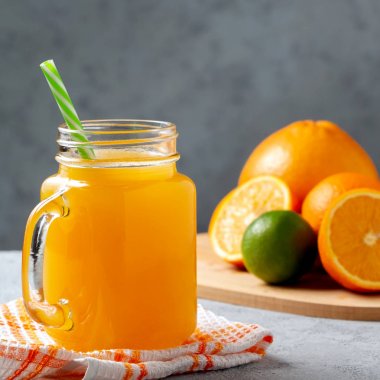 Taze yapılmış narenciye suyu portakal, greyfurt ve limon gri masada bir saman ile bir kavanoz-kupa içinde