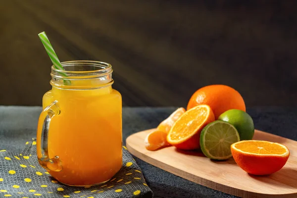 Freshly made citrus juice from oranges, grapefruit and lime in a jar-mug with a straw on black table — Stock Photo, Image