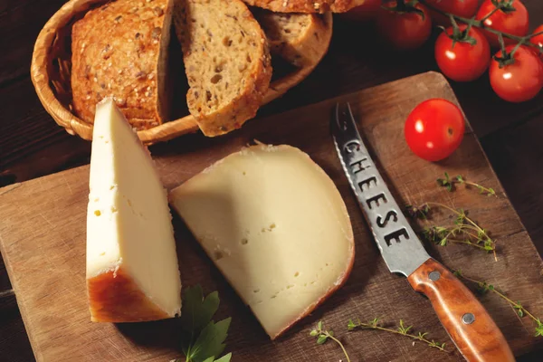 Cortar una rebanada de queso duro, tomillo, cuchillo de queso, pan de grano y tomates cherry en una mesa de madera — Foto de Stock