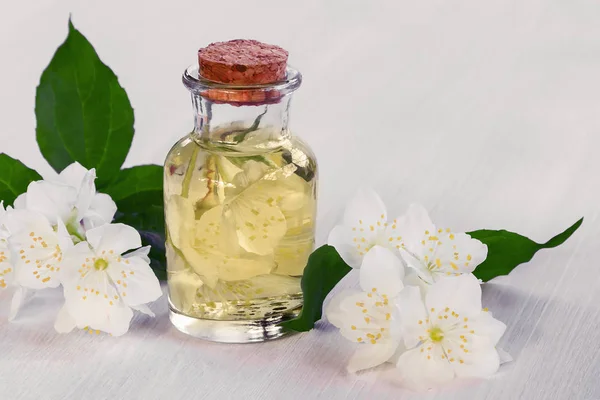 Blüten des Philadelphus irgendwo genannt Jasmin oder Scheinorange und eine Flasche Öl auf einem weißen Holztisch — Stockfoto