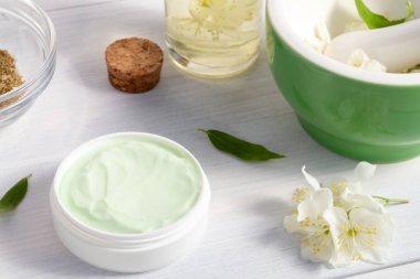 Krem kavanoz doğal bitki maddeler, yağlar ve otlar, yasemin çiçekleri, harç ve havaneli beyaz ahşap arka plan yapılmış - organik kozmetik kavramının hazırlanması