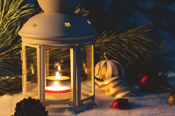 Latarnia z płonącym świecą i dekoracjami świątecznymi na pokrytym śniegiem stole — Zdjęcie stockowe