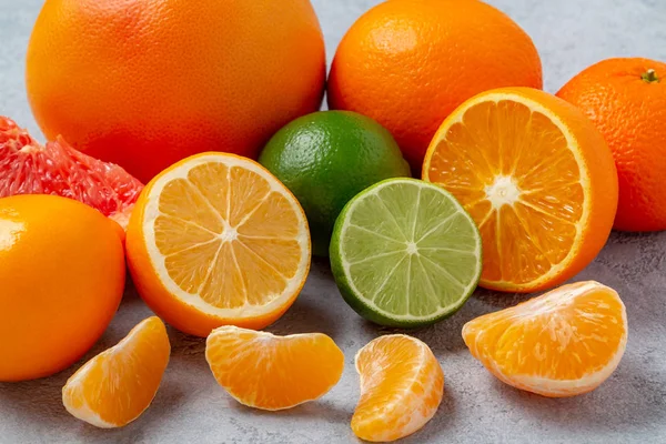 Grupo de citrinos inteiros e fatiados - tangerinas, limões, limas, laranjas, toranjas na superfície da mesa cinzenta - imagem — Fotografia de Stock