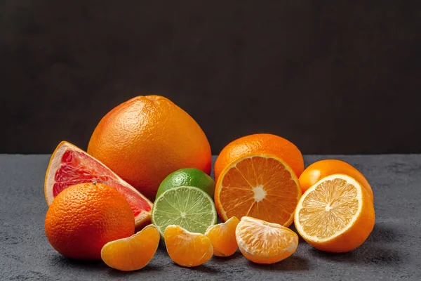 Grupo de frutas cítricas - tangerinas, limões, limas, laranjas, toranjas na superfície de uma mesa cinza contra uma parede preta - imagem com espaço de cópia — Fotografia de Stock