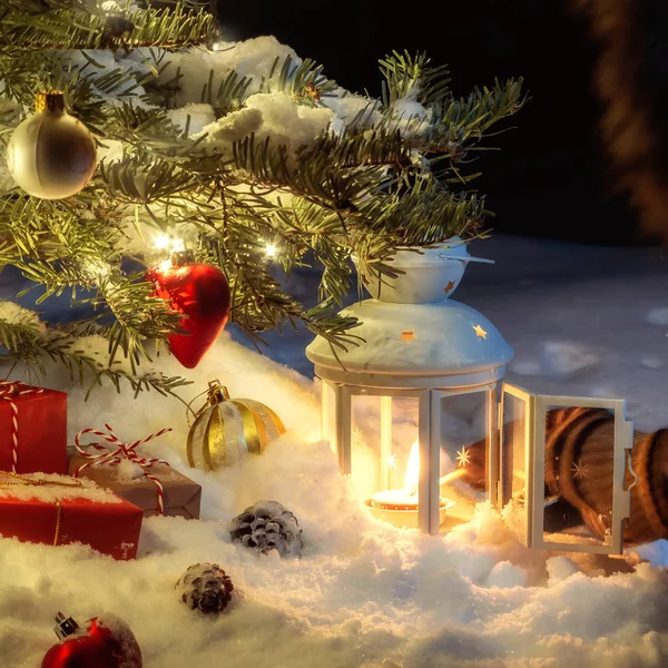 Composición navideña: un árbol en la nieve, regalos, decoración y una mano encendiendo una linterna con una cerilla — Foto de Stock