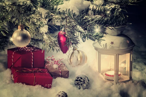 Tarjeta de Navidad - regalos y una linterna en la nieve bajo un árbol de Navidad decorado con luces y decoraciones de Navidad — Foto de Stock